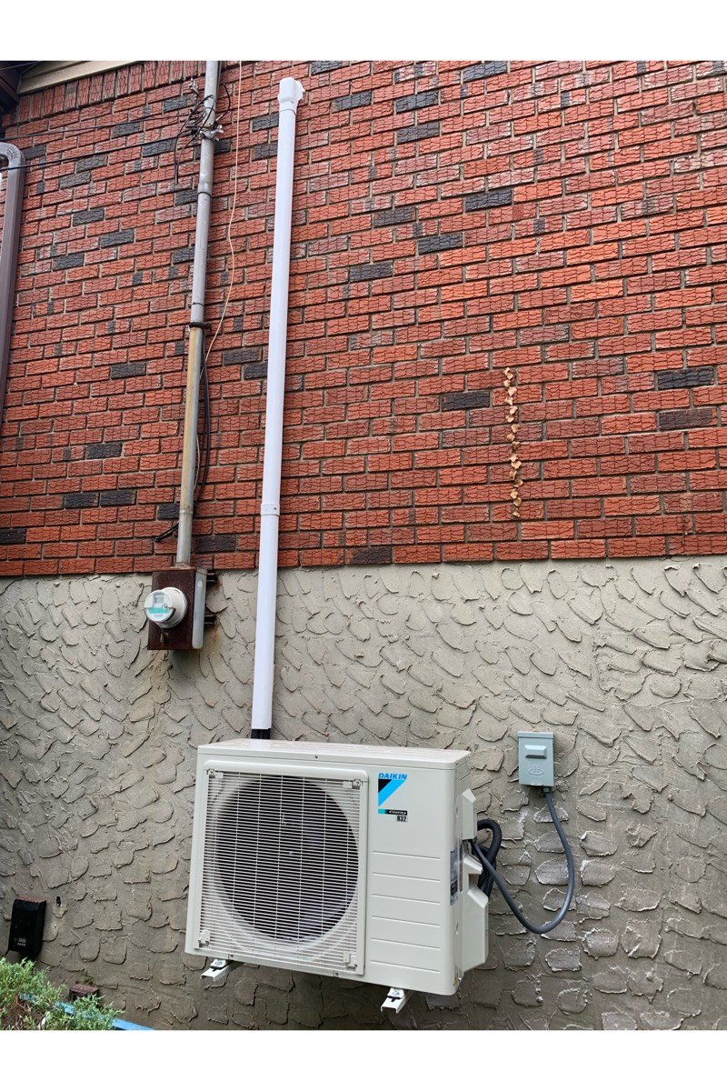Daikin outdoor unit mounted on wall brackets, with line-set cover and electrical disconnect