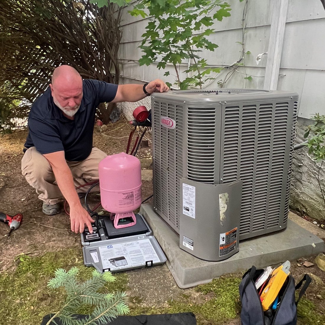 LNL technician servicing a Lennox outdoor condenser with recovery cylinder and scale